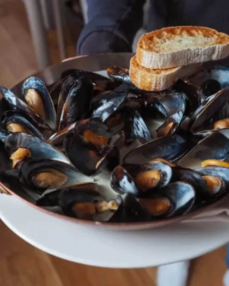 En gryde muslinger med ristet brød, der bliver båret ud til bordet