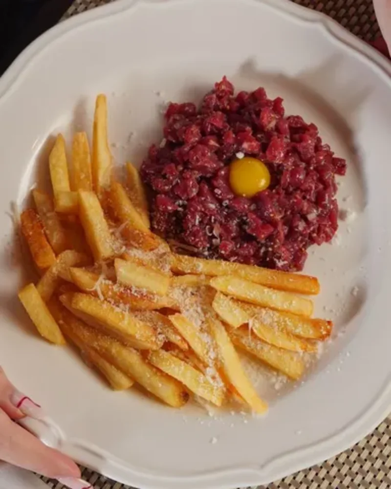 Tatar med æggeblomme og pommes frites i hånden på en gæst